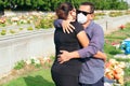 Husband with protective mask trying to comfort his wife in a cemetery. Tragic results of the coronavirus