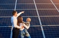 Husband shows his family the solar panels on the background. Blond child in arms of wife.