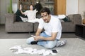 Husband sitting on the floor with many bills and calculating expenses of his wife who sitting on the couch Royalty Free Stock Photo