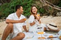 husband and wife chatting holding drink glasses sitting on a blanket picnicking
