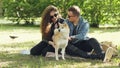 Husband and wife happy couple are fussing their pet shiba inu puppy sitting on grass in park and talking. Conversation