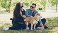 Husband and wife happy couple are fussing their pet shiba inu puppy sitting on grass in park and talking. Conversation