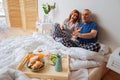 Husband and wife laughing and eating breakfast in bed