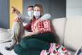 Husband and wife siting on couch with protective medical masks