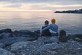Husband and wife sitting on huge stones near the water and hold hands in the evening