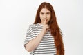 Hush, dont tell anyone. Mysterious redhead girl shushing, make shh sign with finger on lips and smiling, telling secret