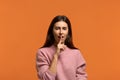 Hush, lets play. Portrait of playful funny beautiful woman in pink sweater with glad expression, keeps index finger over lips,