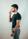 Young man doing hush sign with finger over his mouth, looking at camera