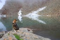Husky sits near a lake in the mountains and looks to the right
