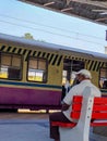 an Indian senior man wearing casual clothing, cap, and mask is seen sitting on a bench wating for train Royalty Free Stock Photo