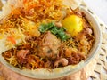 Hyderabadi chicken biryani with tomato, coriander, lemon, cashew nut and bread dum served in copper pot dish isolated on wooden