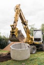 Hydraulic piston system excavator with a bucket, lifting on steel cable concrete sewer ring. Repairs or sewage works on an