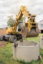 Hydraulic piston system excavator with a bucket, lifting on steel cable concrete sewer ring. Repairs or sewage works on an