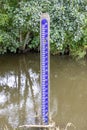 Hydrometric metric scale on Geul river, abundant green foliage in background