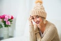 Hygge, comfort and home concept. Young woman in warm beige hand knitted hat at home. Pretty lady in big wool cap, smiling happily Royalty Free Stock Photo