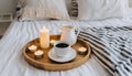Hygge concept Coffee and candle filled wooden tray on a bed accompanied by white bedding striped blanket and pillow serving
