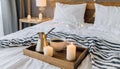 Hygge concept Coffee and candle filled wooden tray on a bed accompanied by white bedding striped blanket and pillow serving