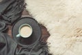 Hygge still life with hot cup of black coffee, warm scarf on furskin and wooden board. View from above