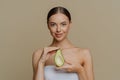 ndoor shot of pleased female model holds half of avocado wrapped in bath towel going to use beauty product nourishes