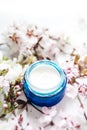 Hygienic skincare lotion product. Herbal spa cosmetic cream with pink cherry flowers in a blue glass jar