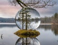 A hyperdetailed image of a glass sphere, inside of which is a tranquil lake, in whose center is a small island on which grows a Royalty Free Stock Photo
