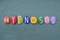 Hypnosis, creative word composed with multi colored stone letters over green sand