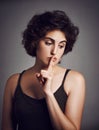 I better keep quiet about this. Studio shot of an attractive young woman with her finger over her lips against a grey
