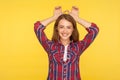 I am bunny! Portrait of carefree cheerful ginger girl in checkered shirt showing rabbit ear over head and smiling, having fun