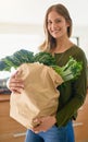 I only buy the freshest produce. Portrait of a smiling young woman standing in her kitchen carrying a paper bag full of Royalty Free Stock Photo