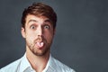 I can be a bit of a goofball. Studio portrait of a handsome young man sticking his tongue out against a dark background.