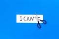 I can concept. Motivate youself, believe in yourself. Sciccors cut the letter t of written word I can`t. Blue background Royalty Free Stock Photo