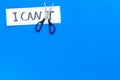 I can concept. Motivate youself, believe in yourself. Sciccors cut the letter t of written word I can`t. Blue background Royalty Free Stock Photo