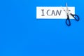 I can concept. Motivate youself, believe in yourself. Sciccors cut the letter t of written word I can`t. Blue background Royalty Free Stock Photo