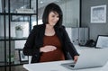 I can feel you moving little one. an attractive pregnant businesswoman sitting in her office and using her laptop while