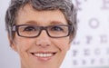 I can see clearly now. Closeup of a mature female wearing glasses standing in front of an eye test poster. Royalty Free Stock Photo