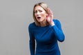 I can`t hear! Portrait of curious attentive woman keeping hand near ear. indoor studio shot isolated on gray background