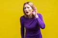 I can`t hear! Portrait of curious attentive woman keeping hand near ear. indoor studio shot isolated on yellow background