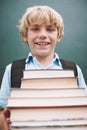 I cant wait to read them all. A cute young boy carrying a large stack of books and smiling at you. Royalty Free Stock Photo