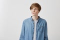 I don`t know. Doubtful caucasian young male wearing denim shirt, pouting lips and looking up with indecisive expression