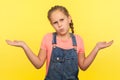 I don`t know! Portrait of clueless uncertain little girl in denim overalls raising hands in questioning gesture