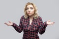I don`t know. Portrait of confused beautiful blonde young woman in casual red checkered shirt standing with raised arms and