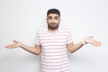 I don`t know. Portrait of confused handsome bearded young man in striped t-shirt standing with raised arms and dont know what to