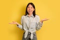 I don't know. Puzzled young Asian woman shrugging shoulders and smiling at camera on yellow studio background Royalty Free Stock Photo