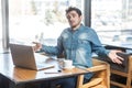 I don`t know! Side view portrait of confused handsome bearded young freelancer in blue jeans shirt are sitting in cafe and making Royalty Free Stock Photo