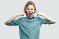 I don`t want to hear this. Portrait of angry handsome long haired blonde young man in blue shirt standing, puting fingers in ears Royalty Free Stock Photo