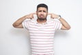 I don`t want to hear. Portrait of sad confused bearded young man in striped t-shirt standing, looking at camera and putting his Royalty Free Stock Photo