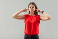 I don`t want to hear you. Portrait of confused brunette young woman in red shirt standing with closed eyes and putting her finger