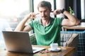 I don`t want to hear you! Young dissatisfied businessman in green t-shirt sitting, looking at laptop screen on video call and Royalty Free Stock Photo