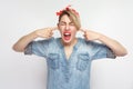 I don`t want to here. Portrait of screaming dissatisfied young woman in blue denim shirt and red headband standing and holding