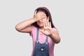 I don`t want to look at this. Portrait of scared or shy girl in pink t-shirt and blue denim overalls standing, covering her eyes Royalty Free Stock Photo